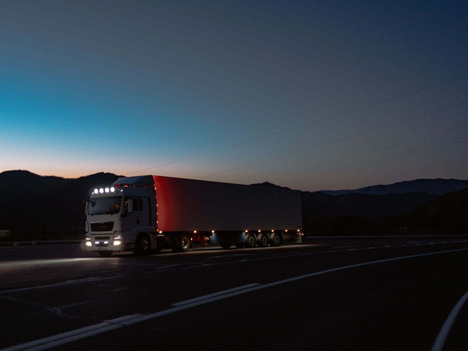 Semi-truck with running lights on rolling in at dusk